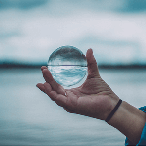 Hand hält Glaskugel über dem Wasser – Symbol für Klarheit, spirituelle Führung und innere Balance