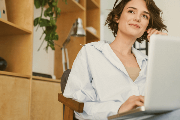 Lächelnde Frau mit Laptop in einem modernen, natürlichen Arbeitsumfeld – wirkt entspannt, inspiriert und fokussiert bei der Arbeit.