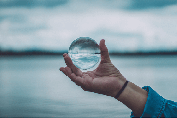 Hand hält Glaskugel über dem Wasser – Symbol für Klarheit, spirituelle Führung und innere Balance