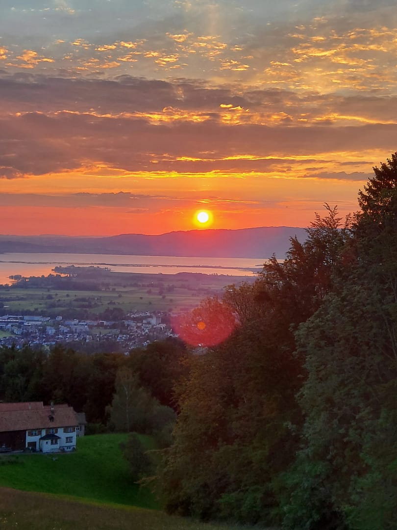 Sonnenaufgang über Wolfhalden mit Blick auf den Bodensee, leuchtender Himmel, grüne Hügel und ein Haus im Vordergrund